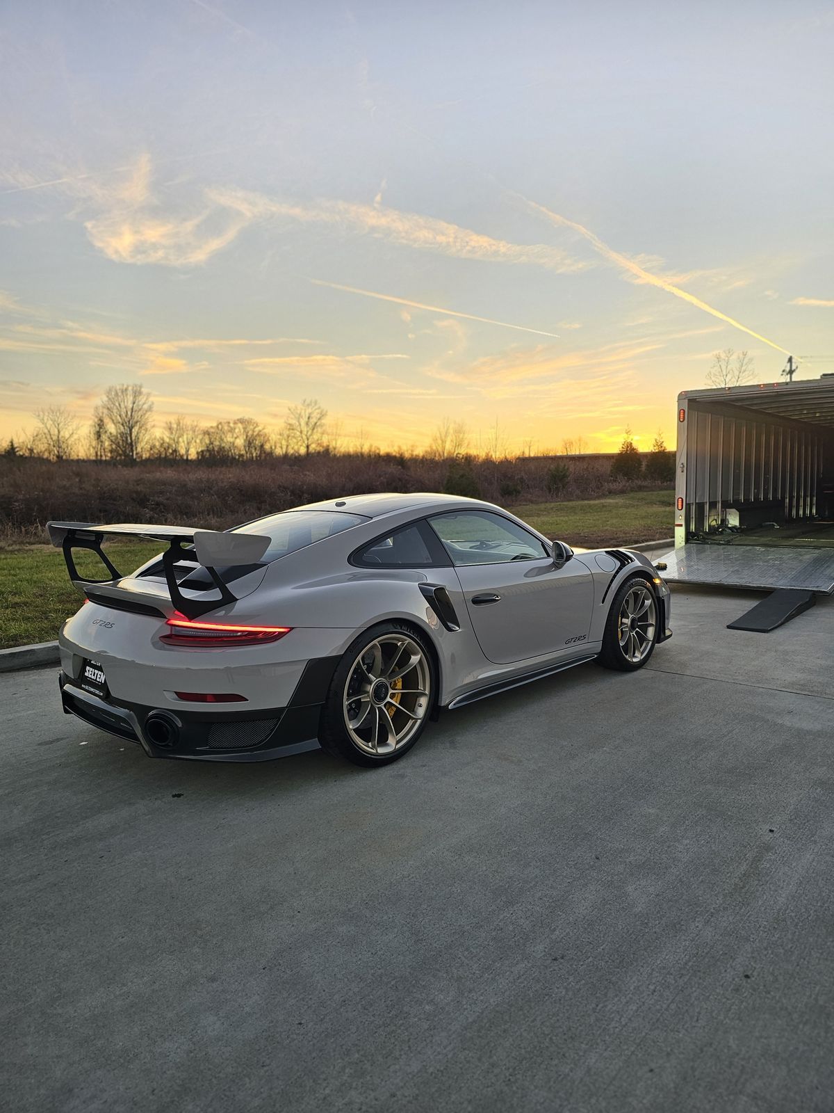 Porsche 911 GT2 RS beside an enclosed trailer at sunset